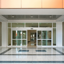 Automatic glass sliding commercial doors at the entrance of a modern building, with tiled floor and bright lighting inside—ideal for businesses seeking professional commercial door installation.